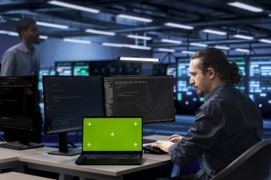 Veri merkezindeki yönetici, izole ekran dizüstü bilgisayarındaki sistem izleme yazılımını kullanarak arızaların kök nedenini belirler. Sunucu çiftliğinde bilişim uzmanı altyapıyı kroma anahtar defteriyle onarıyor