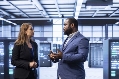 Colleagues doing brainstorming in server hub after installing storage units. IT staff member talking in data center, doing maintenance after replacing mainframes components clipart