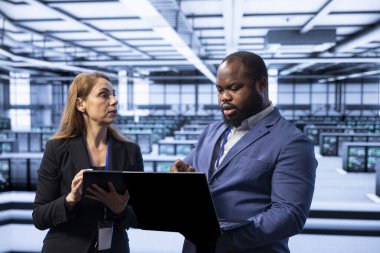 Coworkers in data center using notebook to identify and solve technical issues related to data center infrastructure. Team of admins managing, maintaining and securing server farm environment clipart