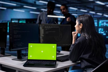 Modern veri merkezinde izole ekran monitörüyle çalışan bir kadın. Yüksek teknoloji ortamında sunucu raflarında bilgisayar kullanarak IT altyapı yönetimi yapıyor.