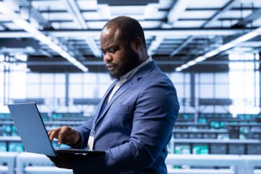 Bilgisayar bilimci, veri merkezindeki laptop 'u gelişmiş teknolojiyle kullanıyor. Siber güvenlik ve etkin ağ yönetimi sağlıyor. Cihazla veri merkezini optimize eden sunucu merkezinde Afrikalı Amerikalı uzman