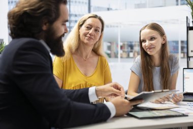 Finansal danışman yatırım performansı hakkında raporlar hazırlayıp anne ve kızına gösteriyor. Aile üyelerine ekonomik evrimin portföyünü sunan temsilci