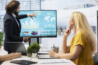 Finansal danışman müşterilere piyasa analizlerini geniş ekran kullanarak sunuyor, veri odaklı karar verme sürecini vurguluyor. Borsa hisseleri hakkında istatistiksel grafikler gösteren aracı