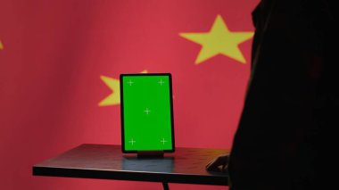 Chinese engineer uses green screen tablet to make fake accounts on social media promoting communist ideology. Technician doing cybersecurity job for CCP government with mockup device, camera A clipart