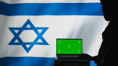 Israel secret police agent uses mass propaganda tools on green screen laptop to influence population minds and spread misinformation. Mossad spy commits PsyOp sabotage using mockup notebook, camera B clipart