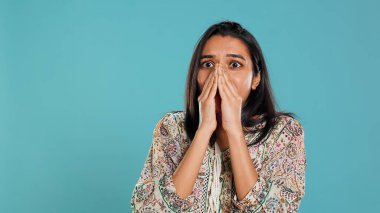 Anxious indian woman covering face with palms, worried about future, isolated over studio background. Tense person shocked by troubling news, gasping, feeling distressed, camera B clipart