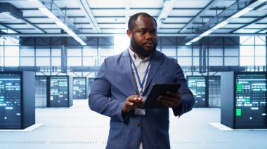 IT technician walking in data center, overseeing server operations using tablet. Expert ensuring optimal performance and data integrity in server hub using digital device, camera B clipart