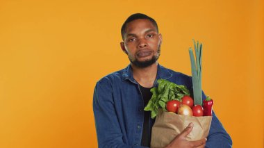 Afro-Amerikan bir adamın portresi. Elinde bir torba dolusu biyolojik yiyecek var. Yerel olarak yetiştirilmiş organik meyve ve sebzeler alıyor. Sağlıklı beslenmeyi destekleyen kendine güvenen vejetaryen insan ve sıfır atık. Kamera A.