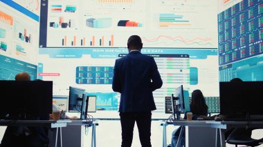 Büyük ekrandaki önemli veri görselleştirmelerini inceleyen idari asistan, kilit performans göstergeleri ve iş verimliliğini gözden geçirmek için bir analiz oluşturdu. Kamera B.