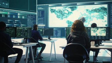 Bir grup hükümet korsanı bir ağı ele geçirmek için hackleme araçları kullanıyor, siber savunma ve veri koruma önlemlerine odaklanıyor. Uzman ekip büyük ekranda önemli bilgileri inceliyor. Kamera B.