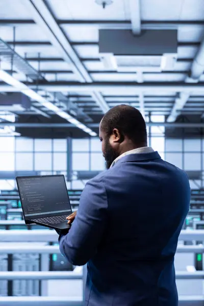 stock image Data center manager ensuring safety and security of database using notebook. African american man in server farm preventing unauthorized access and suspicious activities posing risks for business