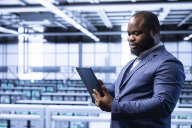 Sistem yöneticisi, veri merkezinde gelişmiş teknolojiyle tablet kullanarak siber güvenliği ve etkili ağ yönetimini sağlıyor. Sunucu merkezindeki adam cihaz ile veri merkezi ekipmanlarını optimize ediyor