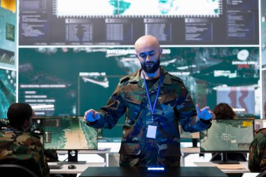 Askeri personel, kumanda merkezindeki hologram projeksiyonunu inceliyor, yeni bir savunma planı üzerinde çalışıyor. Asker gerçek zamanlı CCTV uydu verilerine holografik bir görselleştirmede bakıyor..