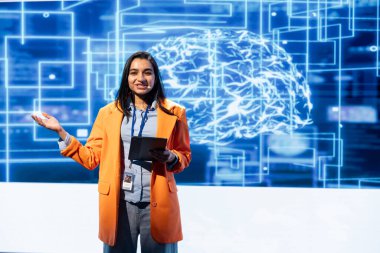 Yapay Zeka Teknolojisi Zirvesi 'nde sunum yapan neşeli mühendis tablet kullanan profesyoneller topluyor. Yeniliği hızlandırmak için yapay zekanın nasıl kullanılabileceğini göstermek için aygıt kullanan neşeli konuşmacı