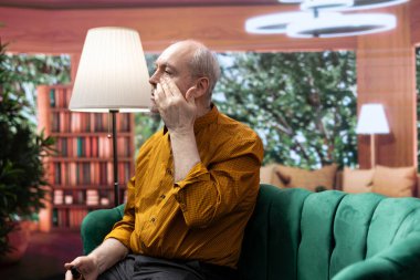 Yaşlılık ve kırışıklıklarla mücadele ederken, yaşlı yüzüne bakım ürünleri uygulamak için ayna kullanan yaşlı bir insan. Adam günlük rutinini ultraviyole koruma kremi ve serumla yapıyor..