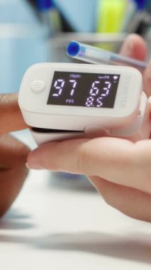 Dikey video uzmanı, hastasıyla rutin bir kontrol sırasında oksijen doygunluğu ölçümünü alır ve hayati belirtileri kontrol eder. Sıhhiye ofisteki doğru okumalar için bir oksimetre kullanıyor