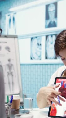 Dikey Video Kadın uzmanı test sonuçlarında kalp fonksiyonlarını ve durumunu, doktor hasta etkileşimini kabinede açıklıyor. Doktor kardiyolog tabletteki kardiyovasküler sistemi gösteriyor