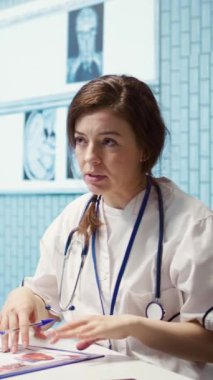 Dikey Video Sağlık Uzmanı tıbbi uzmanlığını kabinedeki bir hastayla paylaşıyor, röntgen ve MRI taramalarını inceliyor ve doğru tanı ve hasta bakımına odaklanıyor. Teşhis raporu