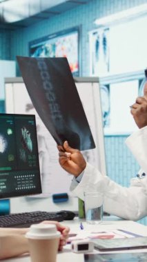 Dikey Video Medikal uzmanı, kontrol altındaki hastaya röntgen görüntüleme test sonuçlarını gösteriyor, tedavi hakkında tartışıyorlar. Doktor, yorumlama ve tanı raporları için radyografi taramalarına bakıyor.