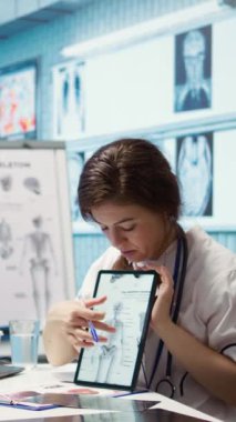 Dikey video sağlık sağlayıcısı kabinedeki bir hastaya laboratuvar sonuçlarını sunuyor, röntgen ve MRI taramalarını inceleyerek iyileşme sürecinde yardımcı oluyor. Teşhis ve bakımda tıbbi teknoloji