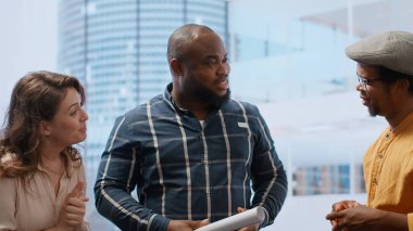 Emlakçı ve müvekkil, ofis turu sırasında mimari planlar değerlendirmesine odaklanarak kira anlaşması üzerinde görüşüyorlar. Potansiyel alıcı yenileme görüşünü paylaşıyor. Kamera B.