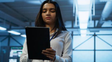 Yazılım geliştiricisi veri merkezinde yürüyor, tablet kullanarak dişli tasarlıyor, uyguluyor ve yönetiyor, optimum performans ve güvenilirlik sağlıyor. Sunucu çiftliğindeki IT çalışanı cihaz üzerinde kodlama yapıyor, kamera A