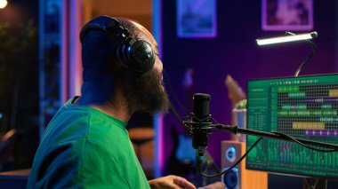 Kendine güvenen sanatçı, ses dosyalarını kaydetmek ve profesyonel kurgu yazılımında ham sesi manipüle etmek için mikrofonla şarkı söylüyor. Müzik prodüksiyonu. Kamera A.