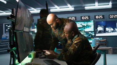 Military dispatcher helped by coworker with tablet to gain info from army intelligence analysts. Army intelligence corps expert discussing with colleague in command post, camera B clipart