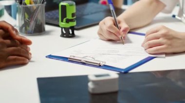 Yetenekli bir doktor, kontrol altındaki erkek hastaya tıbbi ilaçlar ve ağrı kesiciler yazarak geçerlilik damgası ile reçete yazıyor. Doktor sigorta belgesini imzalıyor. Kamera A.