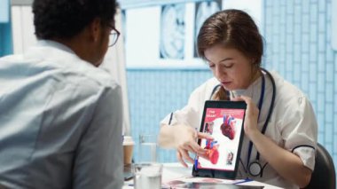 Sağlık hizmeti sağlayıcısı kardiyolog kalp fonksiyonlarını bir kardiyogramda, doktor hasta etkileşimini bir tıp ofisinde açıklıyor. Sağlık ekibi olası durumu vurguluyor, kardiyovasküler sistem. Kamera A.