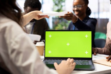 CEO, iş ortaklarıyla yaptığı toplantıda proje geliştirme sürecini gözden geçirmek için yeşil ekranlı dizüstü bilgisayar kullanıyor. Stratejik hedefleri sağlamak için detaylı analiz ve modellemeler kullanılıyor.