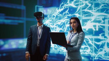 VR kulaklık takan teknisyenler, meslektaşlarının da yardımıyla bilgisayar kullanarak yapay zeka insan beyni simülasyonuna bakıyor. Yapay Zeka görselleştirmesi ile etkileşim halinde olan programcı takımı, kamera B