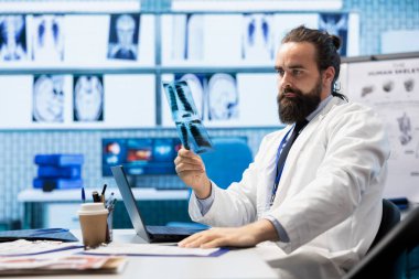 Genel pratisyen hekim röntgen taramalarını ve klinikteki test sonuçlarını inceliyor, hastalık önleme için en iyi tedavi planını laptopta hastane kayıtlarıyla birlikte çalışıyor. Radyoloji uzmanı.