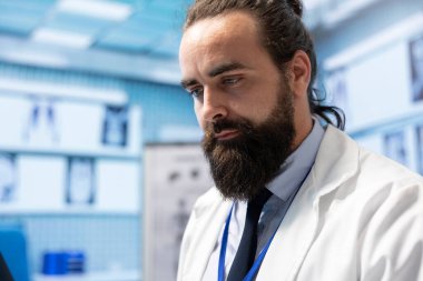 Tıp kabinesinde dizüstü bilgisayar üzerinde çalışan genel uzman bir doktor, sağlık kayıtları ve profesyonel hastalık önleme tedavisi için yeni test sonuçlarını karşılaştırıyor. Masada doktor var. Kapat..