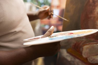 Güzel sanat galerisi için güzel bir başyapıt yaratmak için resim tekniğini kullanan Afrikalı Amerikalı ressam, tuvale uygulamadan önce palette suluboya boyaları karıştırıyor. Sanatsal atölye. Kapat..
