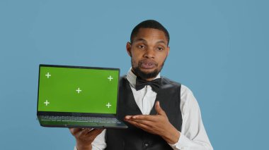 Kapıcı çocuk stüdyoda elinde yeşil ekranlı bir laptop tutarken beş yıldızlı bir otelde konukseverlik sektöründe çalışırken izole edilmiş krom anahtar görüntüsünü sunuyor. Profesyonel personel. Kamera A.