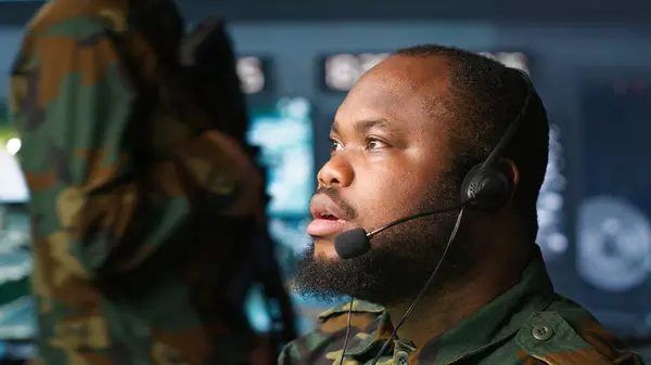 stock image Military dispatcher relays info from army intelligence analysts to troops on front lines, close up shot. Radio communications operator wearing uniform talking in headset mic, camera A