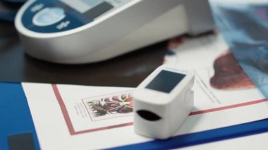Profesyonel ve temiz tıp bürosu, oksitölçer, tansiyon monitörü ve teşhis araçları ile donatılmış, sağlık hizmetleri ve modern teşhisleri vurgulayan bir hasta muayene muayenesini bekliyor..