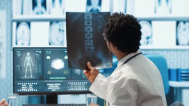 Hekim MRI taraması ve röntgen sonuçlarını muayene ediyor. Hastanın muayenehanesinde. Teşhisi açıklıyor. Doktor, hastalığı ve tıbbi teknolojiyi tartışmak için analizi işaret ediyor. Kamera A.