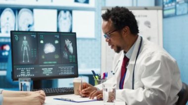Doktor, kabinedeki kadın hastaya sağlık sigortası ve sağlık hizmetleri hakkında teşhis raporunu açıklıyor. Afrikalı Amerikalı doktor müşterilerine tavsiye ve geri bildirim veriyor. Kamera A.