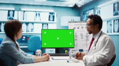 Afrika kökenli Amerikalı tıp uzmanı bilgisayar ekranında bir kadına danışarak tarama yorumu için ekranı işaret ediyor. Erkek uzman profesyonel tavsiye veriyor. Kamera B.