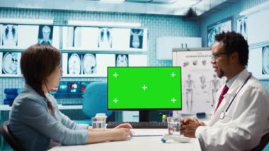 Afro-Amerikan tıp uzmanı bir hastayla fotokopi makinesine bakıyor, tesisteki kabine danışmanlığına katılıyor. Erkek uzman, sağlık sigortası için bir tedavi öneriyor. Kamera B.