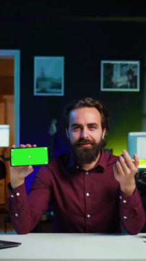 Dikey video adam yeşil ekran cep telefonunu gösteriyor, boş bir kopya alanı olarak kullanarak çevrimiçi yayın kanalı logosunu gösteriyor. Medya yıldızı krom anahtar telefon, kamera B kullanarak giriş videosu yapıyor