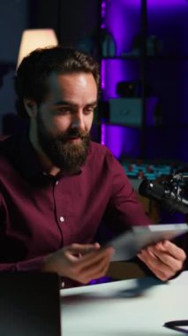 Dikey video teknisyeni, düşük bütçeli tableti ilgili izleyicilere sunuyor, akıllı telefonuyla tripodla çekiyor. Dijital aygıtı inceleyen adam, cep telefonuyla kayıt yapıyor