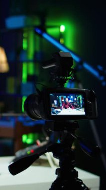 Bulanık arka plandaki adam tarafından kullanılan profesyonel kamera üzerine dikey video odak noktası Neon lit Stüdyoları 'nda internet şovu sunuyor. Vlogger 'ın yayın sırasında kullandığı yüksek teknoloji ekipmanlarını kapat