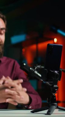 Dikey video ASMR sanatçısı stüdyoda tripodun üzerinde kaliteli mikrofon ve akıllı telefon kullanarak stres karşıtı videolar yapıyor, fısıldayan sesler çıkarıyor. Uyutma için mikrofon ve cep telefonu kullanan bir adam.