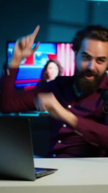 Dikey video dışavurumcu medya yıldızı mikrofonu kullanarak video çekiyor, çılgınca hareketler yapıyor. Ev stüdyosunda profesyonel mikrofonla video bloğu çekerken enerji etkileyicisi hareketli el hareketleri yapıyor