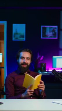 Stüdyoda gülümseyen etkileyici bir dikey video yayımcıdan yeni çıkan ciltli kitabı inceliyor. Yazardan okuyucuya yeni bir roman sunan mutlu akademisyen edebiyat videosu denemesi çekiyor