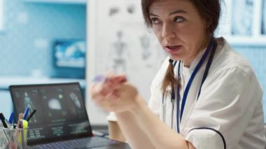 Hekim, bir kabinede tıbbi sonuçları tartışmak için bir hastayla buluşur. Röntgen taramalarını yorumlamak için gelişmiş teşhis cihazları kullanarak profesyonel bir sağlık yaklaşımı gösterir. Kamera A.