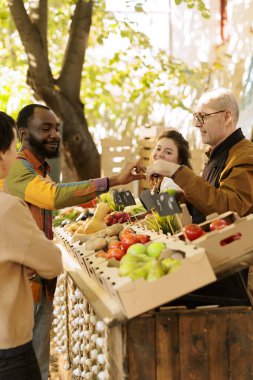 Çiftçilerin pazarında taze ürün tatmış siyah bir adam, meyve ve sebze satan yaşlı bir adam ev yapımı ürün sunuyor. Yaşlı çiftçi, yerel markette organik bahçe ürünleri satıyor..